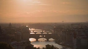 Veduta aerea panoramica del tramonto sul fiume Arno a Firenze, che proietta un bagliore dorato sui suoi ponti iconici, con Ponte Vecchio in primo piano. Tucci in Italy - Toscana