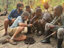 Kerllen Costa, Dr. Steve Boyes, and a group of Angolan tribal hunters check Steve's cellphone video of a ghost elephant at their search camp